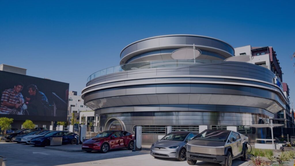 The retro-futuristic Tesla Diner building with a long line of Tesla vehicles parked outside.